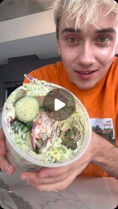 a young man holding a bowl of food with cucumbers and onions in it