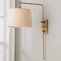 a wall lamp with a white shade on it next to a window in a room