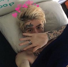 a man with tattoos on his arm laying in bed next to a teddy bear and pillows