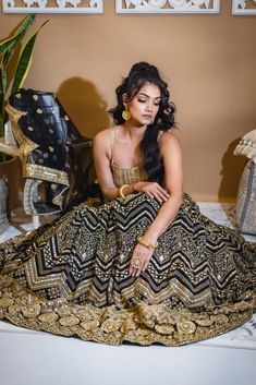 Loyla - Black Georgette Lengha & Gold Silk Choli w/ Mirror & Bead Embroidery If elegance had to be visually depicted then this black and gold lehenga choli would speak volumes with its sophistication! Gold dupion silk choli w/ sequins & bead handwork Breathable golden Dupion silk blouse Graceful scoop neckling choli blouse Beaded trim detail at neck & hemline Gorgeous sequin & bead embroidery Sweetheart back neck with tie-up Dori Flowy black georgette lehenga w/ mirror embroi Black Traditional Wear With Gold Embroidery For Festive Occasions, Traditional Black Gown With Zari Work, Black Dupatta With Gold Embroidery In Traditional Drape, Bollywood Style Black Dupatta With Gold Embroidery, Party Black Dupatta With Gold Embroidery, Black Traditional Wear With Gold Embroidery For Wedding, Gold Embroidered Lehenga For Party And Festivals, Festive Black Gown With Zari Work, Party Lehenga With Gold Embroidery For Festivals