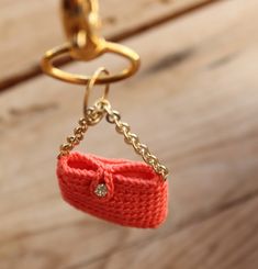 an orange knitted purse hanging from a gold chain on a wooden surface with a keychain attached to it