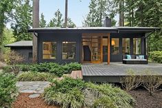 a black house with lots of windows and wood flooring in the front yard is surrounded by greenery