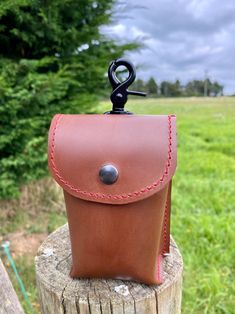 a brown leather case sitting on top of a tree stump with a black metal hook in it