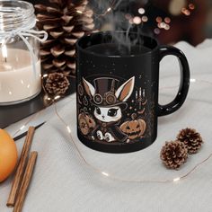 a black coffee mug sitting on top of a table next to candles and pine cones