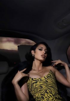 a woman in a yellow and black dress is sitting in a car with her hand on her hip