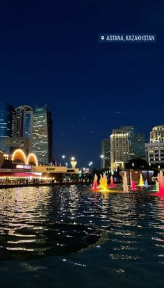 there are many fountains in the water at this city's riverfront park and it is lit up with brightly colored lights