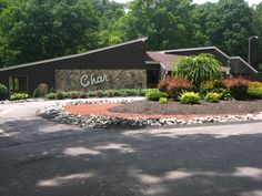 the entrance to an office building with landscaping and trees around it, in front of a parking lot