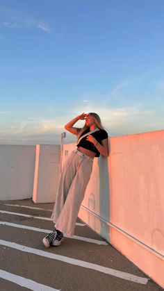 a woman leaning against a wall with her hand on her head and looking at the sky