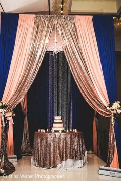 a wedding cake is on top of a table with blue and pink draping