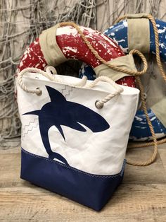 "NEW SHARK DESIGN! Vintage sails upcycled into one-of-a-kind totes!  Each bag is handcrafted from select sails on hand so no two totes are exactly alike. Weathering of the sails bestows characteristics unique to each bag.  Shoulder Bag measures approximately 16\"w x 12\"h x 6\"d and includes three open interior pockets.  Handcrafted from recycled sail and paired with a navy marine canvas on the bottom.  A full top zipper closure and water resistant liner give added protection to your belongings.   Rope handles and a large navy shark add a nautical flair to this lightweight and durable shoulder bag.  Handles have a 9\" drop for over the shoulder comfort.  Select from two handle colors, natural or navy! Easy care instructions:  Treat with spot remover if needed.  Hand wash with warm water an Upcycled Beach Tote Bag, Upcycled Tote Bag For Beach, Nautical Beach Bag In Sail Color, Nautical Sail-colored Beach Bag, Nautical Style Beach Tote Bag, Nautical Sail-colored Bag For Daily Use, Nautical Style Sail-colored Bag For Daily Use, Nautical Sail Color Bag For Daily Use, Nautical Style Sail Color Bags For Daily Use