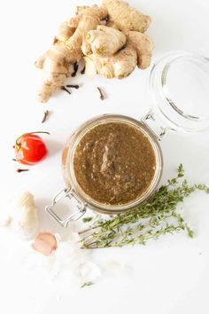 a jar filled with brown sauce next to garlic, tomatoes and other ingredients on a white surface