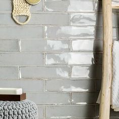 a gray brick wall with two crocheted hats hanging on it and a wooden stool