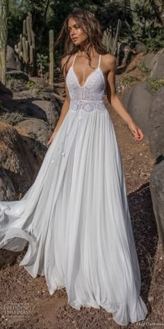 a woman in a white dress is walking through the desert with cacti and rocks