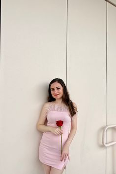 a woman in a pink dress leaning against a wall with a rose on it's side