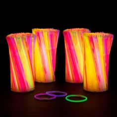 four different colored vases sitting on top of a black table next to neon rings