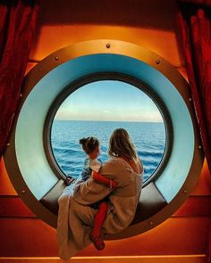 a woman and child looking out at the ocean through a porthole in a ship