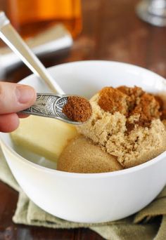 a person holding a spoon in a bowl with some food inside of it on top of a table