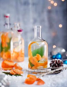 two bottles filled with liquid and orange slices on top of snow next to christmas decorations