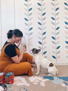 a woman sitting on the floor playing with her dog while she is painting wallpaper