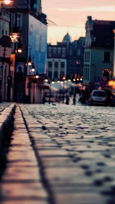 an empty cobblestone street at dusk with people walking on the sidewalk and buildings in the background