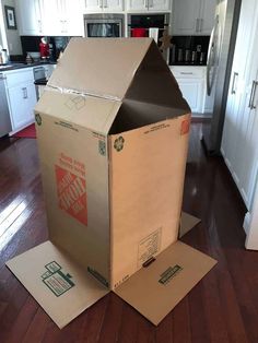 an open cardboard box sitting on the floor in front of a kitchen with white cabinets