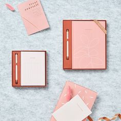 three pink notebooks, one with a notepad and the other with a pen