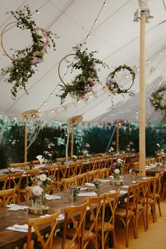 tables and chairs are set up in a tent for an outdoor wedding reception with hanging floral wreaths