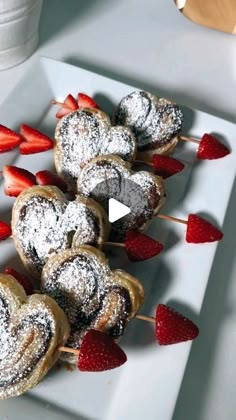 strawberries and powdered sugar covered pastries on a white plate with toothpicks in the shape of hearts