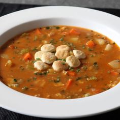 a white bowl filled with soup and dumplings on top of a black place mat