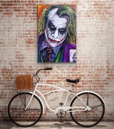 a painting of the joker on a brick wall next to a white bicycle with a basket