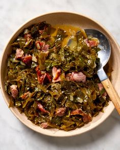 a bowl filled with greens and meat on top of a white countertop next to a wooden spoon