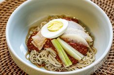 a white bowl filled with noodles and meat on top of a woven tablecloth covered place mat