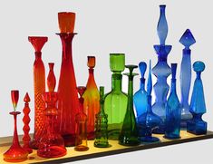 there are many different colored glass vases lined up together on the shelf in front of each other