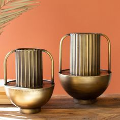 two metal vases sitting on top of a wooden table next to a planter