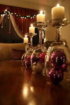 three wine glasses filled with christmas balls and candles on a table in front of a couch