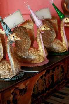 three golden swan figurines with hats on their heads are lined up against a pink wall