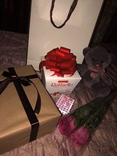 a teddy bear sitting next to a box with a red ribbon on it and two roses