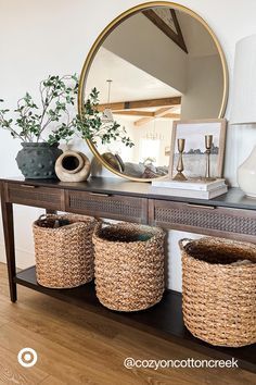 a console table with three baskets and a round mirror on the wall above it in a living room