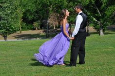 a young man and woman in formal wear holding hands while standing on the grass near trees