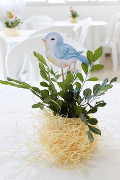 a small blue bird sitting on top of a plant in a vase filled with straw