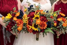 three bridesmaids in red dresses holding bouquets of sunflowers and roses