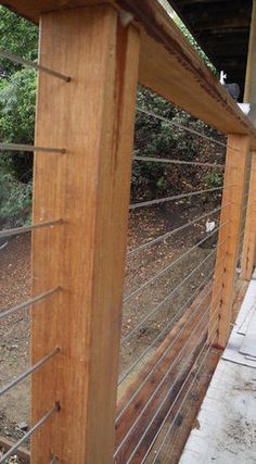 a close up of a wooden fence with wire on the top and bottom, along with trees in the background