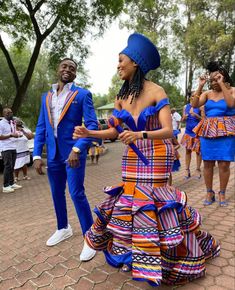 two men in blue and orange outfits dancing on the street with other people behind them