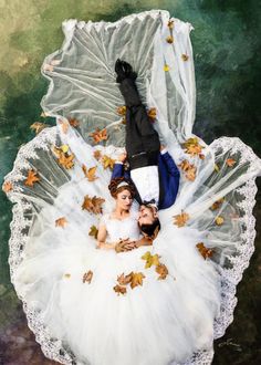 two people laying on top of each other wearing white dresses and veils with leaves all over them