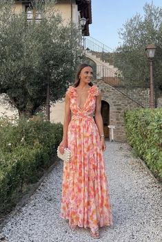 a woman standing in front of a house wearing an orange and pink flowered dress