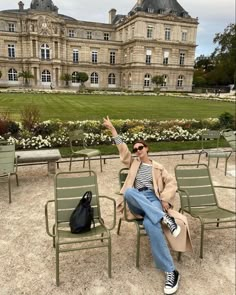 a man sitting on top of a green chair in front of a large building with lots of windows