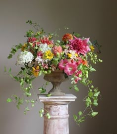 a vase filled with lots of flowers on top of a white pedestal next to a wall