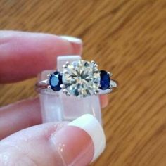 a person holding a ring with three stones in it on top of a wooden table