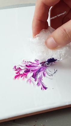 a person is holding something in their hand while they are painting flowers on a plate