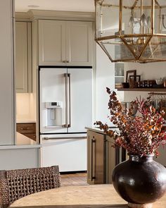 a vase with flowers sitting on top of a table next to a refrigerator freezer